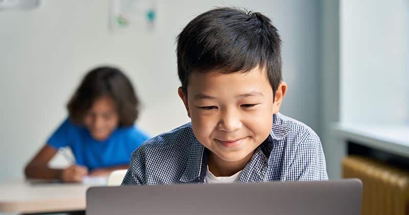 Smiling boy using computer in class